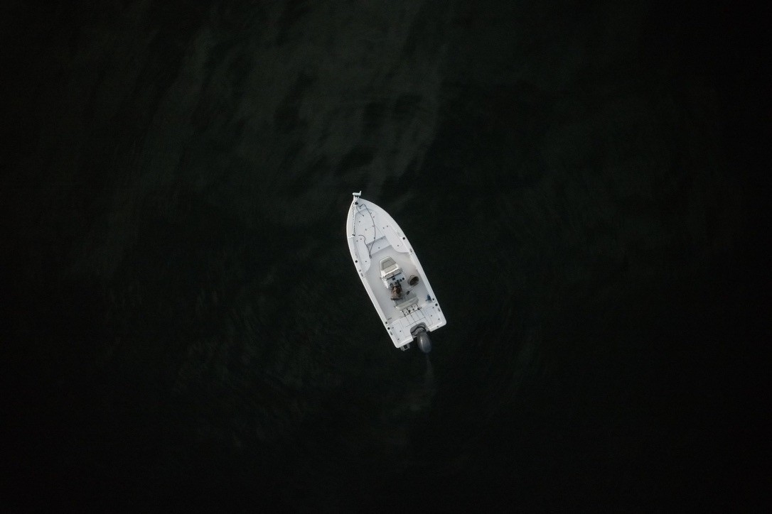 A small white fishing boat seen from above on dark water